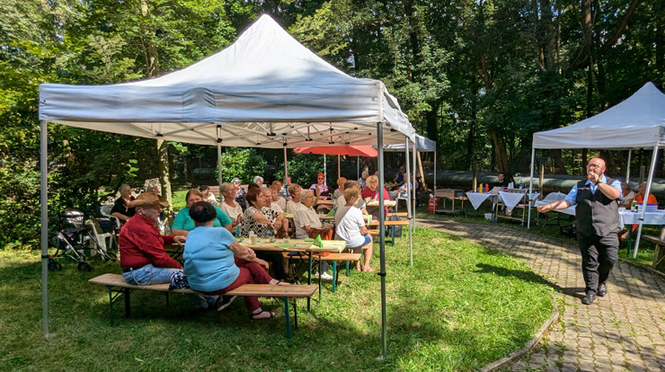 Unter Pavillons sitzen Menschen im Park und hören einem Sänger zu.